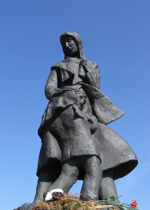 Bronzestatue „He büst blieven“ in Dornumersiel zeigt Frau mit Kind, vor blauem Himmel.
